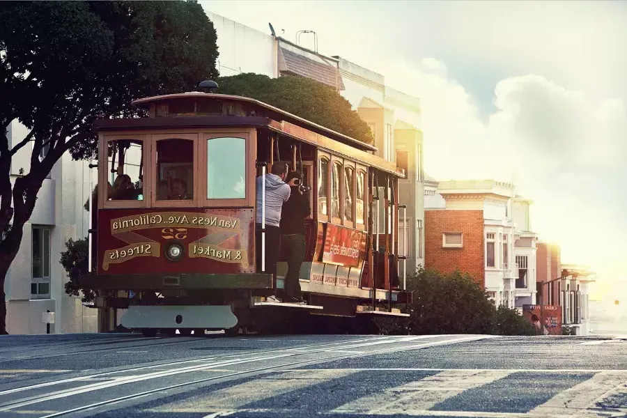 Un tranvía rodea una colina en San Francisco con pasajeros mirando por la ventana.